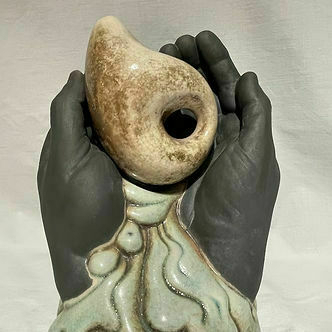 A primitive-looking teapot being held in clay hands